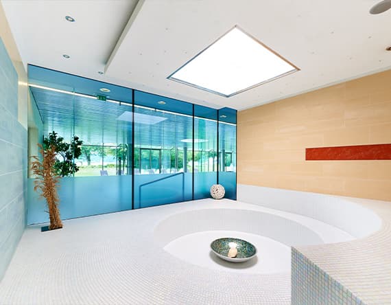 Modernes Spa mit rundem Becken, großen Fenstern und heller Einrichtung. Pflanzen und Dekoobjekte ergänzen das Ambiente.