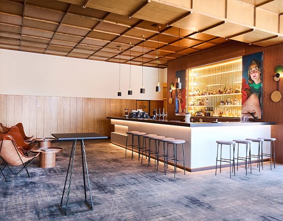 Moderne Bar mit langer Theke und hohen Hockern, Regale mit Alkoholflaschen, gemütliche Sitzbereiche und Kunst an der Wand