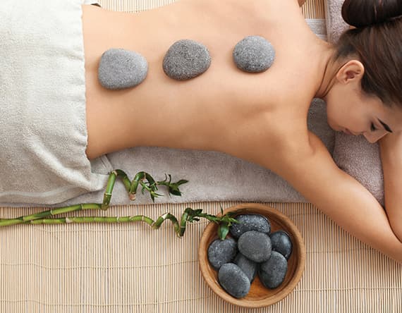 Frau liegt auf dem Bauch, drei Steine auf dem Rücken, daneben Bambus und Schale mit weiteren Steinen