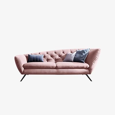 Rosa Sofa mit schräger Rückenlehne, Rautensteppung und mehreren Deko-Kissen vor weißem Hintergrund