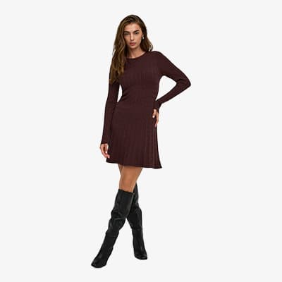 Frau im bordeauxfarbenen Langarmkleid steht mit einer Hand in der Taille und trägt kniehohe schwarze Stiefel