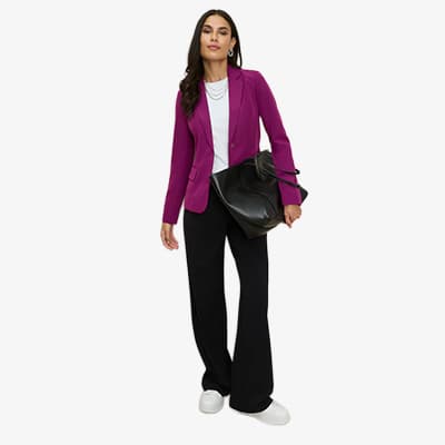 Frau in pinkem Blazer, weißem Shirt und schwarzen Hosen trägt große schwarze Tasche und weiße Sneaker