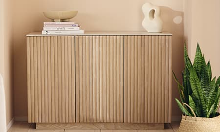 Niedriges Sideboard mit senkrechten Lamellen, dekoriert mit Büchern, Schale und Skulptur, daneben hohe Zimmerpflanze