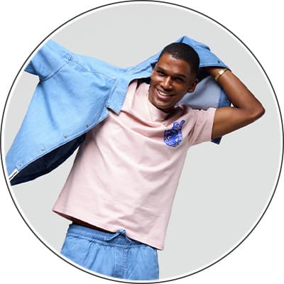 Mann zieht hellblaue Jeansjacke über rosa T-Shirt mit blauem Aufdruck an