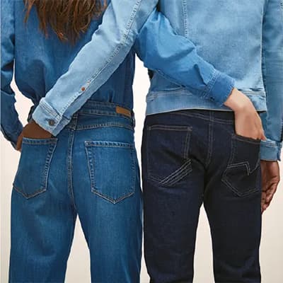 Zwei Personen in Jeans und Jeanshemden stehen mit dem Rücken zur Kamera und haben jeweils eine Hand in der Hosentasche des anderen