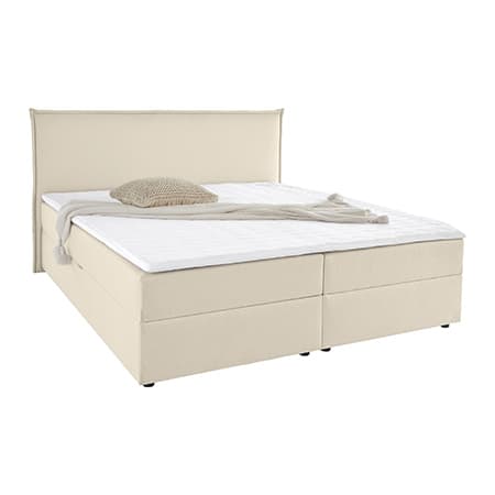 Beiges Bett mit hohem Kopfteil, darauf liegen eine beige gestrickte Decke und ein passendes Kissen