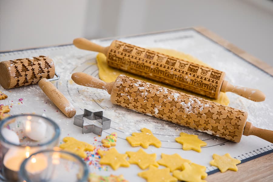 Weihnachtliche Teigrollen mit Sternen, Tannenbäumen und Mustern. Ausgestochene Plätzchen auf einer bemehlten Arbeitsfläche.