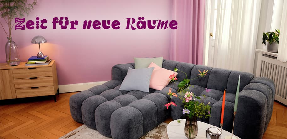Zeit für neue Räume – Wohnzimmer mit grauem Sofa, bunten Kissen und Blumen auf einem Tisch