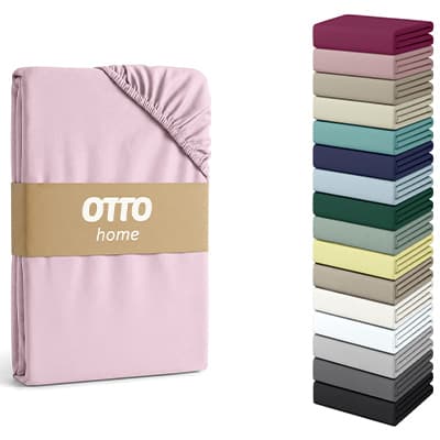 Otto home Spannbettlaken in Rosa, daneben Stapel von Laken in verschiedenen Farben