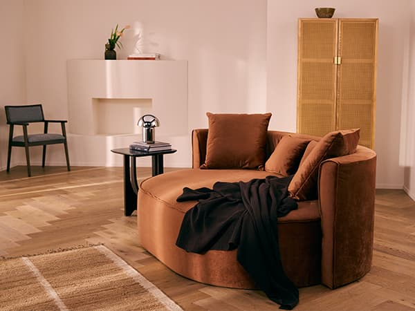 Rundes Sofa mit Kissen und Decke in modernem Wohnzimmer mit Beistelltisch, Stuhl, Teppich und Raumteiler