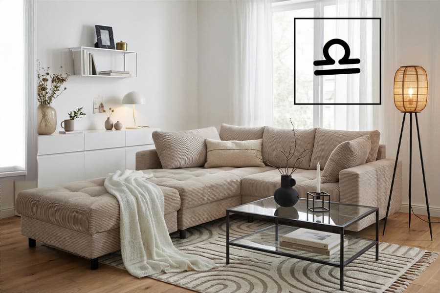 Waage-Symbol an der Wand über beigem Ecksofa mit Decke, Couchtisch aus Glas und Stehlampe im hellen Wohnzimmer