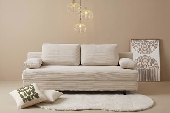 Sofa mit zwei Kissen, davor Teppich mit Zierkissen „good vibes live here“, Wandbild und drei hängende Lampen