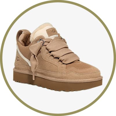 Beiger UGG-Sneaker mit breiten Schnürsenkeln und dicker Plateausohle vor olivgrünem Hintergrund