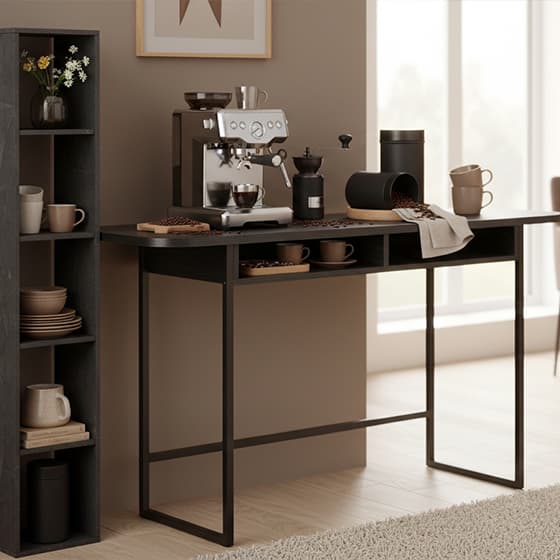 Kaffeestation mit Espressomaschine auf schwarzem Tisch, Mühle, verstreuten Bohnen und Bechern vor hellem Fenster