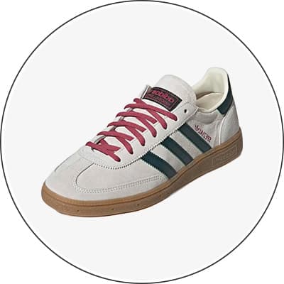 Heller Sneaker mit dunkelgrünen Streifen und roten Schnürsenkeln, seitlich von schräg oben vor weißem Hintergrund gezeigt