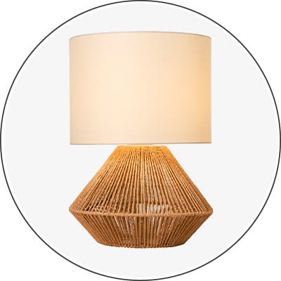 Tischlampe mit breitem hellem Zylinderschirm und konischer, geflochtener Basis vor weißem Hintergrund