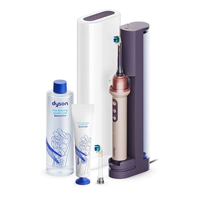 Elektrische Zahnbürste im Ladehalter mit zwei Aufsätzen, Mundspülung und Zahnpastatube von Dyson nebeneinander platziert