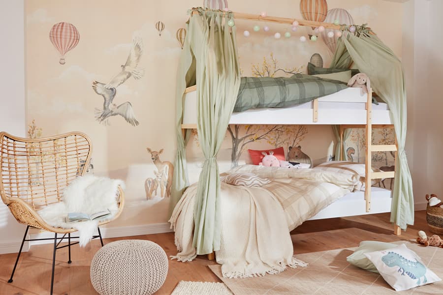 Hochbett mit grünen Vorhängen in Kinderzimmer, Wandgemälde mit Heißluftballons und Vögeln, Rattanstuhl mit Fell, Stofftiere auf Betten