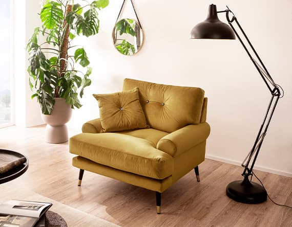 Senfgelber Sessel mit zwei Kissen, Stehlampe, großer grüner Pflanze und rundem Spiegel in hellem Raum