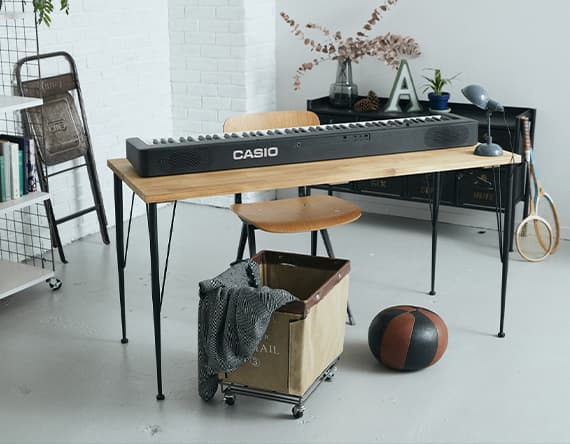 Casio Keyboard auf einem Holztisch in einem Zimmer mit Stuhl, Lampe, Regal, Box, Ball und Tennisschläger