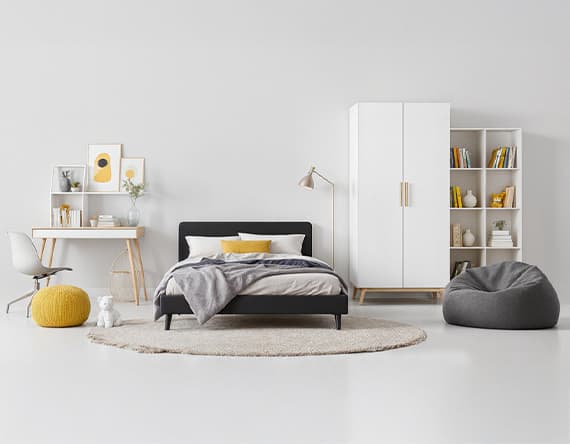 Modernes Jugendzimmer mit Bett, Schreibtisch, weißem Schrank und Bücherregal. Gelber Sitzpouf und grauer Sitzsack auf Teppich.