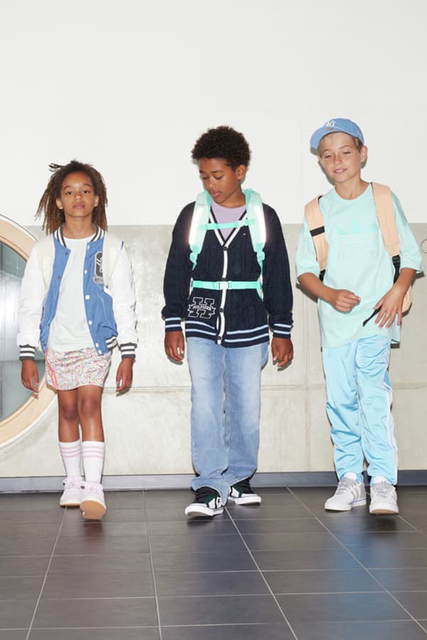 Drei Kinder mit Schulrucksäcken gehen eine Treppe hinauf. Sie tragen lässige Kleidung und haben verschwommene Gesichter.