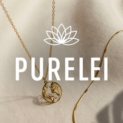 PURELEI – Goldene Halskette mit rundem Anhänger und goldene Armkette auf beigem Stoff drapiert