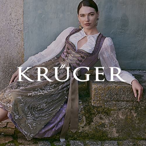 KRÜGER – Frau in traditioneller Tracht lehnt sich entspannt an eine Wand