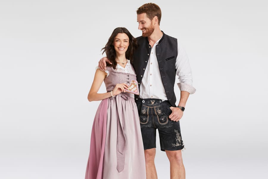 Paar in traditioneller Tracht – Frau in rosa Dirndl und Mann in Lederhosen mit schwarzer Weste und weißem Hemd.