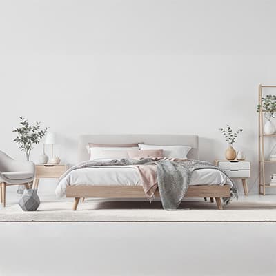 Modernes Schlafzimmer mit Doppelbett, grauer Decke, zwei Nachttischen, Pflanzen, Stuhl und Regal auf hellem Teppich.