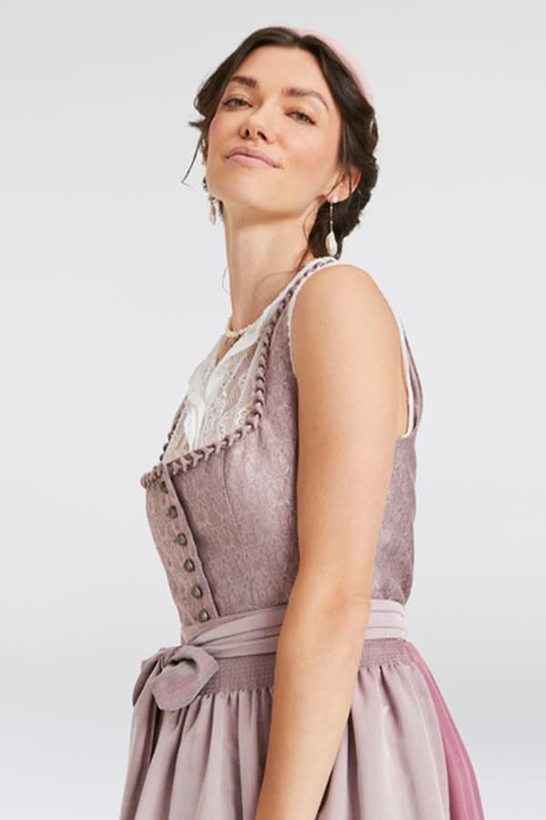 Frau trägt ein rosa Dirndl mit Knöpfen und Spitzenbluse darunter, rosa Schürze gebunden mit Schleife.