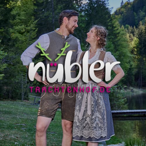 nübler Trachtenmode – Mann in traditioneller Lederhose und Frau in grauem Dirndl stehen in malerischer Waldlandschaft