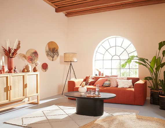 Modernes Wohnzimmer mit orangefarbenem Sofa, großen Pflanzen, runden Wanddekorationen und großem Fenster mit Rundbogen