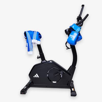 Schwarzes Fitnessbike mit blauen Boxhandschuhen und blau-weißem Trainingsanzug über dem Lenker drapiert