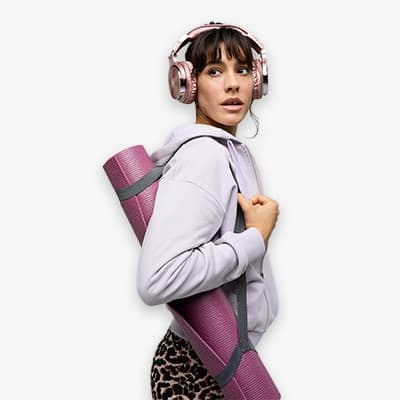 Frau in grauem Hoodie mit rosa Yogamatte und Kopfhörern, trägt Leopardenhose
