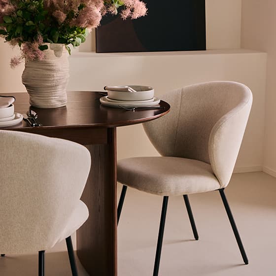 Runder Holztisch mit zwei beigen Stühlen, Vase mit Blumen, gedeckt mit Tellern und Besteck in einem modernen Esszimmer.