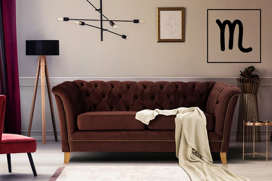 Braunes Sofa mit Kissen und beigem Überwurf, daneben schwarze Stehlampe, rote Sessel, Wandbilder und Deckenleuchte im Hintergrund