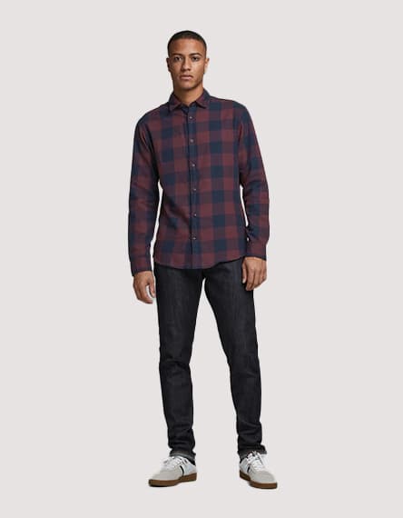 Mann in kariertem Hemd und dunkler Jeans steht frontal, Gesicht ist verschwommen, trägt weiße Sneaker.