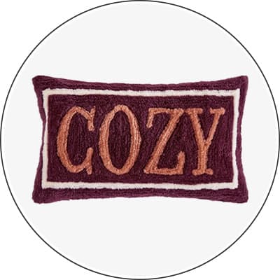 Kissen mit dem Schriftzug "COZY" in orangenen Buchstaben auf lila Hintergrund