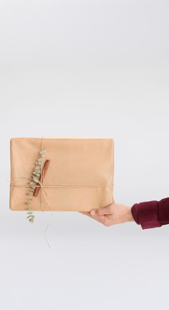 Hand hält braun verpacktes Geschenk mit Zweig und Zimtstange verziert
