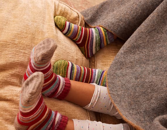 Zwei Paar Füße in bunten gestreiften Socken unter grauer Decke auf beigem Sofa
