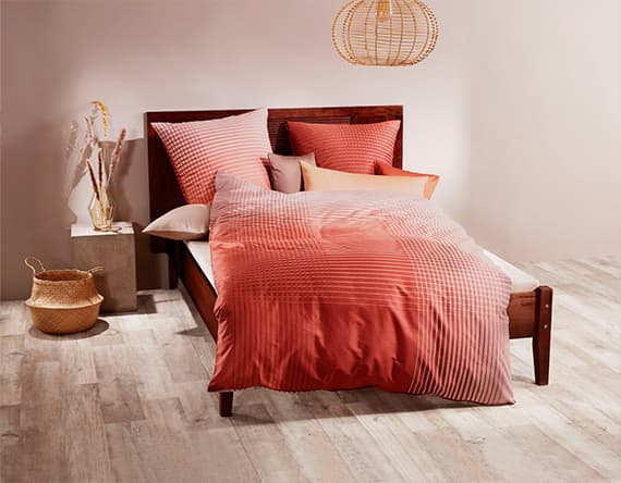 Bett mit rot-gestreifter Bettwäsche, verschiedene Kissen. Holzrahmen, dekorativer Korb und Vase, Hängeleuchte.