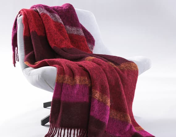 Mehrfarbige Decke in Rot- und Pinktönen liegt auf einem weißen Sessel