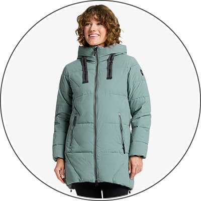 Frau trägt eine lange, grüne Winterjacke mit Kapuze und schwarzen Details. Jacke hat Reißverschlüsse und Taschen.