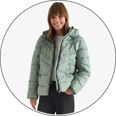 Frau trägt hellgrüne, gesteppte Jacke mit Kapuze, weißes T-Shirt und schwarze Jeans