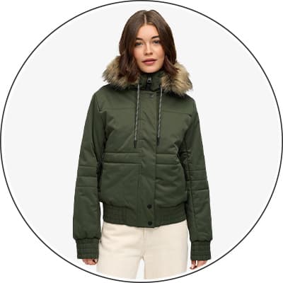 Frau trägt grüne Jacke mit Pelzkragen und weißer Hose, Gesicht unscharf