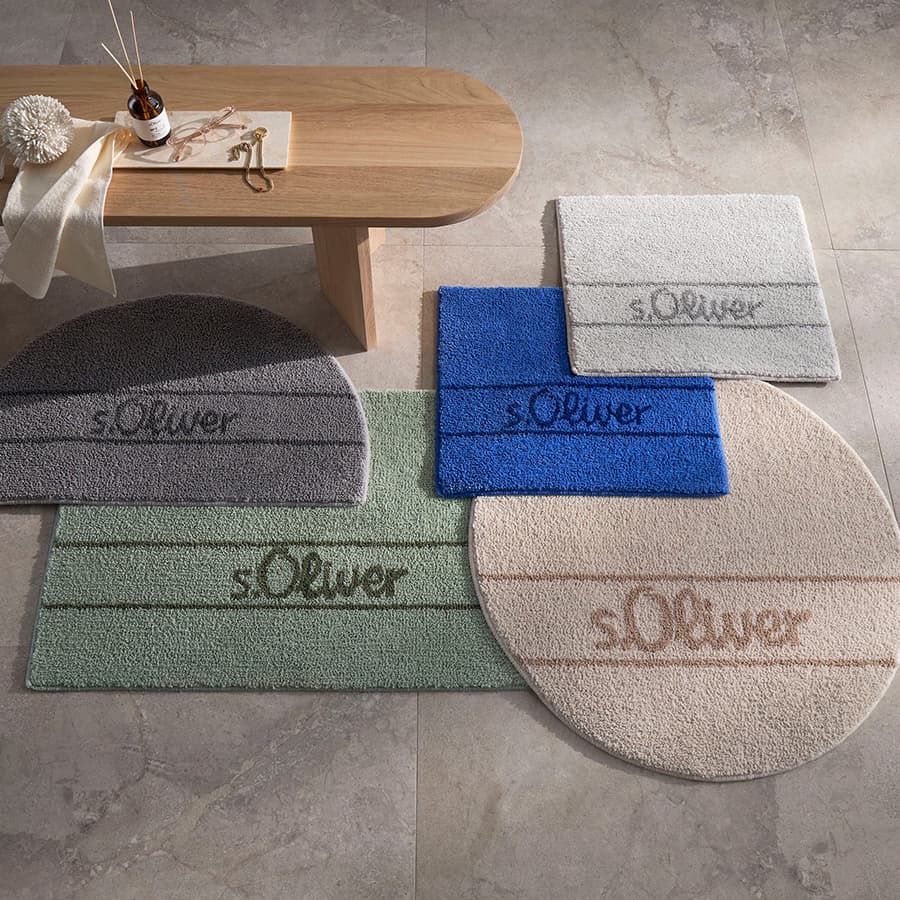 s.Oliver Fußmatten in verschiedenen Farben und Formen auf grauem Boden, daneben Holztisch mit Dekorationen