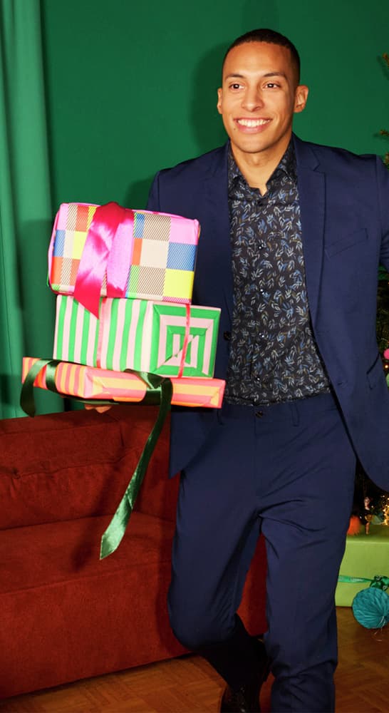 Mann in blauem Anzug hält bunt verpackte Geschenke mit Schleifen vor grünem Hintergrund