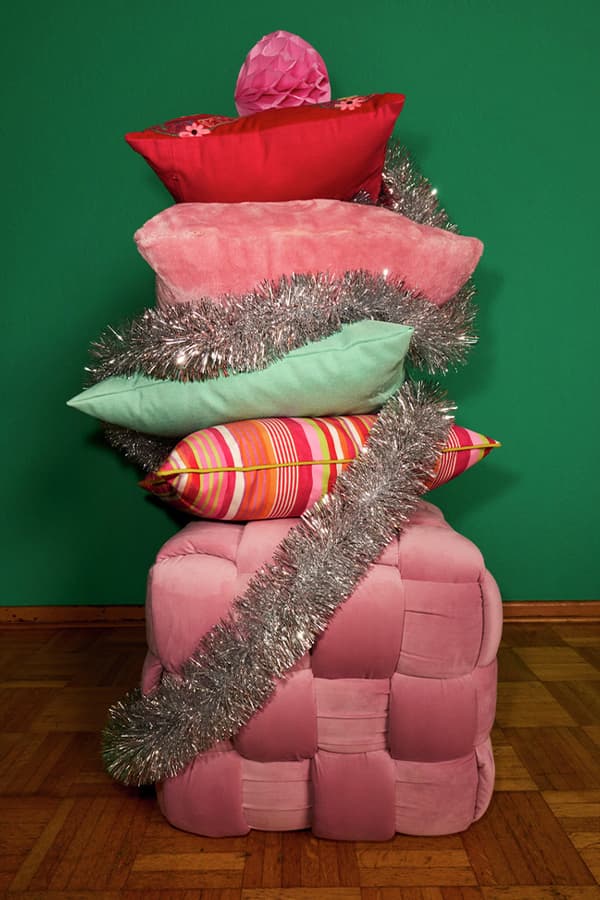 Gestapelte Kissen in verschiedenen Farben und Mustern, dekoriert mit silberner Lametta, vor grüner Wand auf Holzboden