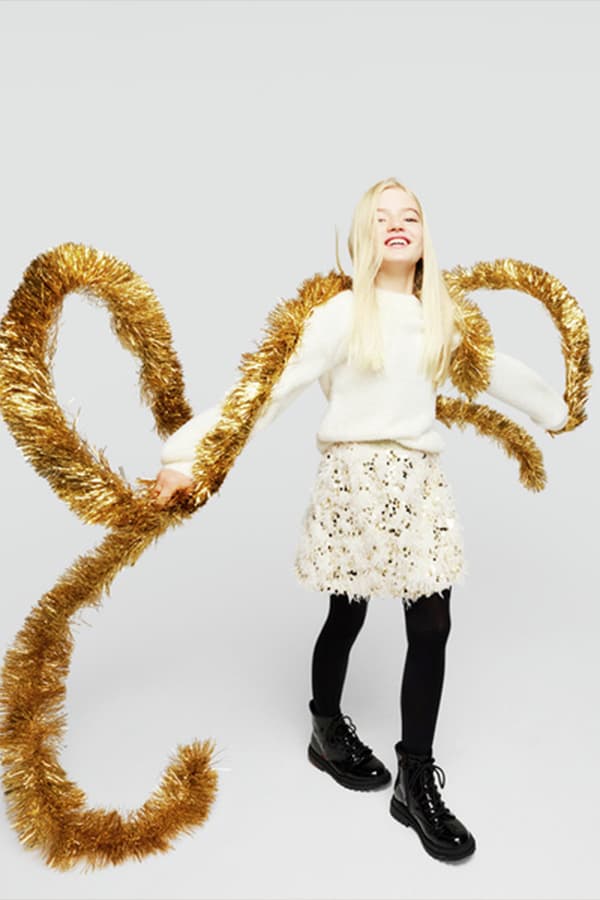 Mädchen mit langen blonden Haaren und festlicher Kleidung hält goldene Girlande in beiden Händen